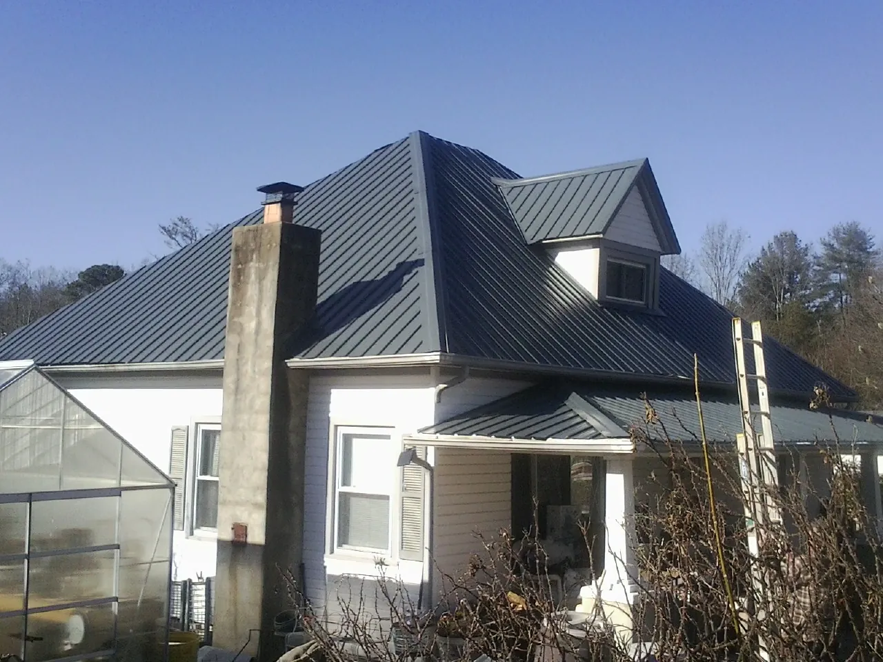 Dark blue standing seam metal roof on a white farmhouse with dormer — Slate & Tile Roof Repair by Roofing Brothers in Rodessa