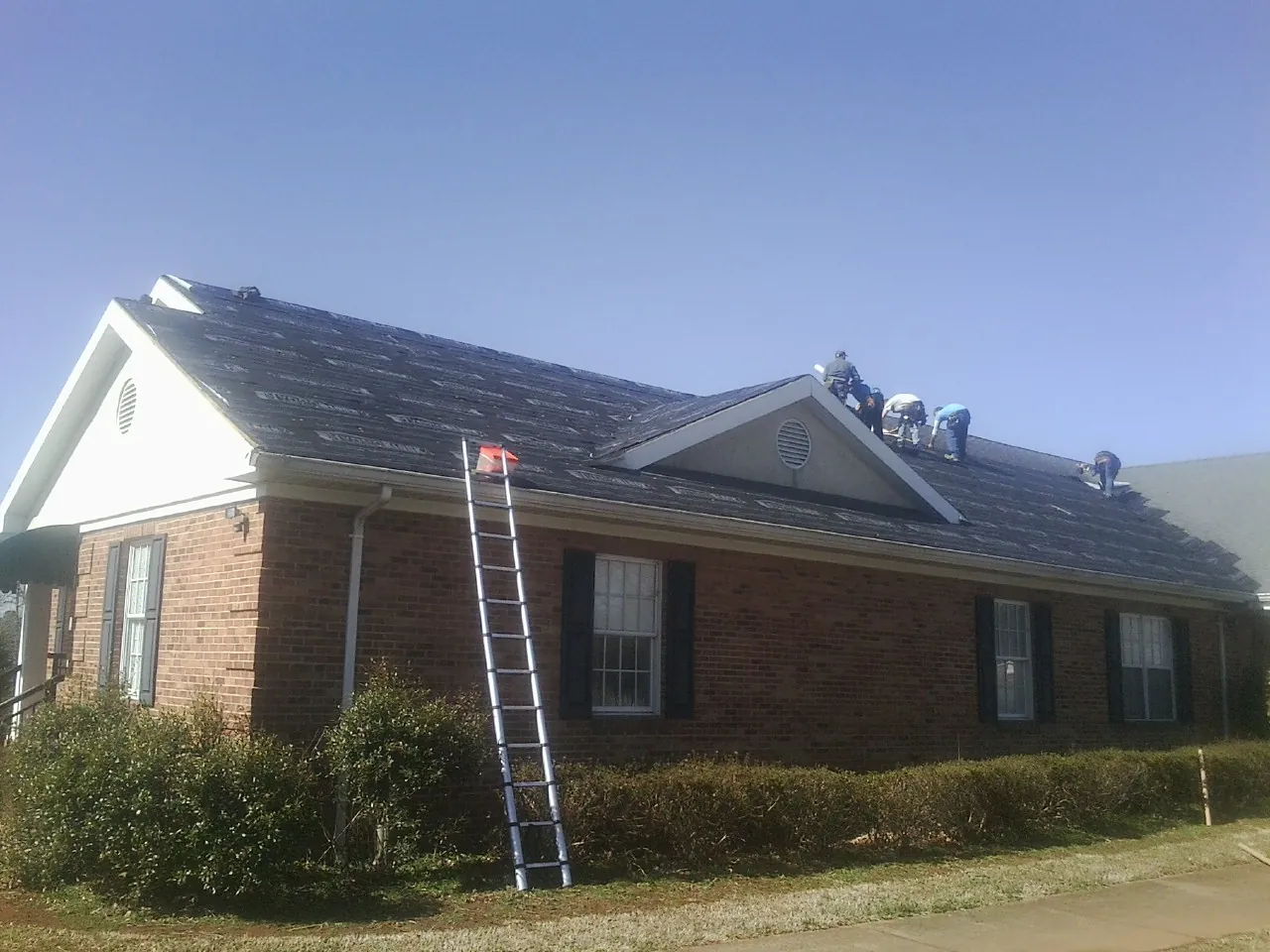 Crew tearing shingles off a brick ranch roof with a ladder set — Metal Roof Repair work by our crew in Rodessa