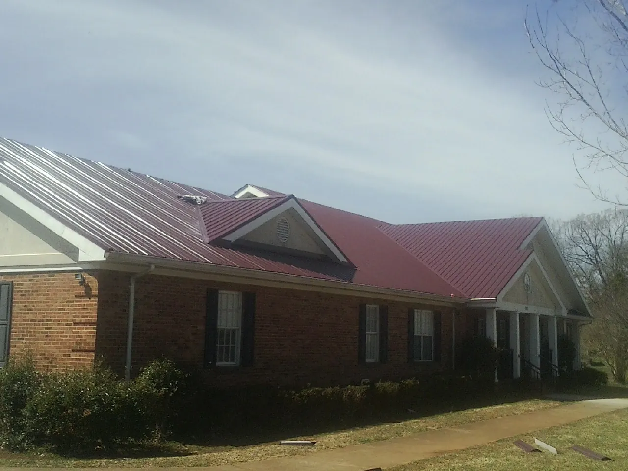 Red metal roof with gabled entries on a long brick building, from a Hail Damage Roof Repair job in Rodessa