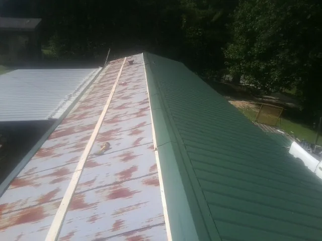 Old rusted panels beside newly installed green metal roofing — Wind Damage Roof Repair by Roofing Brothers in Rodessa