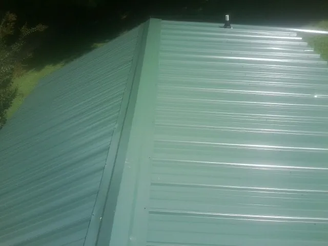 New green metal panels meeting at the ridge of a roof — Flat Roof Repair work by our crew in Rodessa