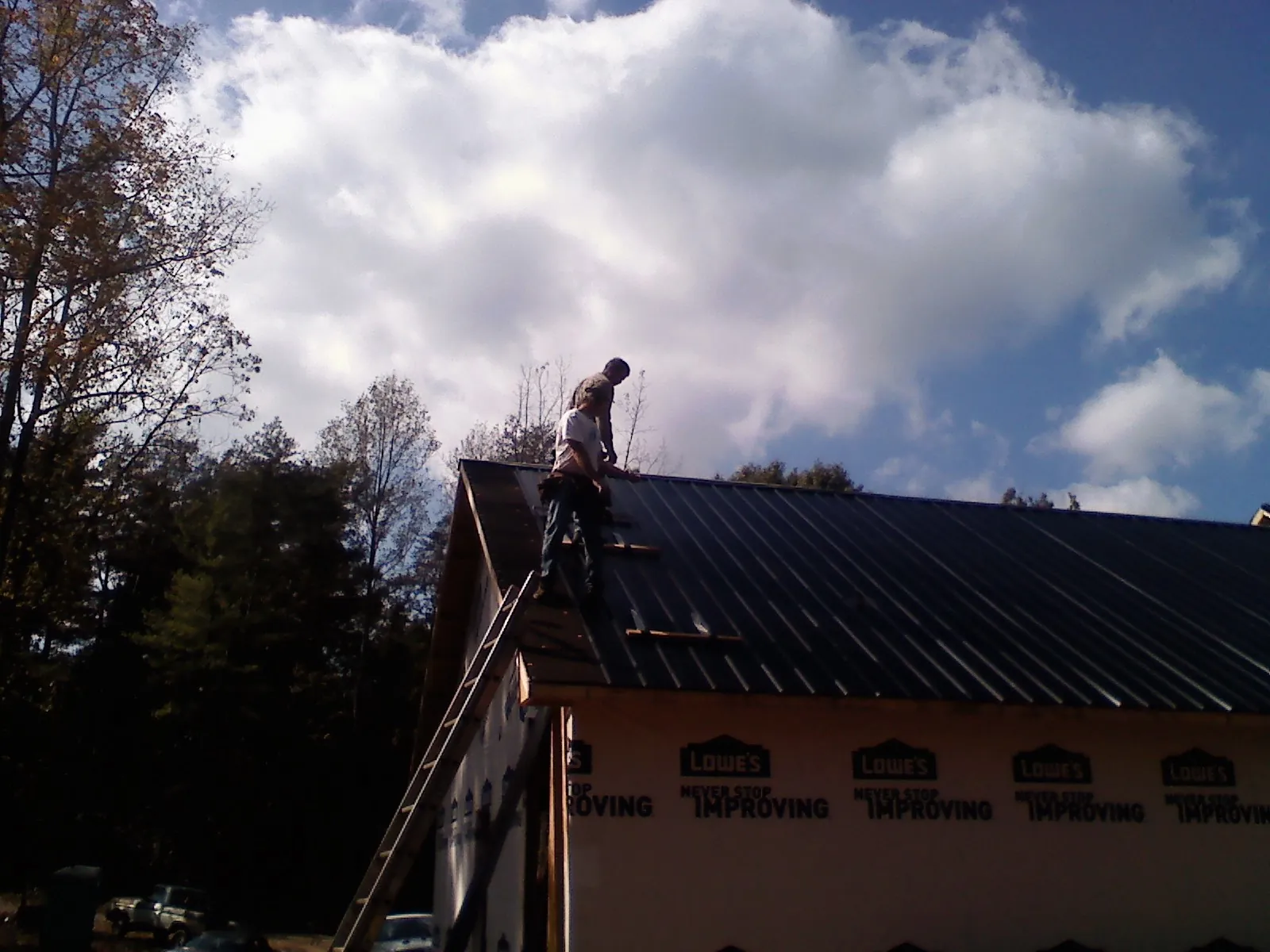 Roofer fastening dark metal panels high against a cloudy sky, from a Roof Inspection job in Rodessa