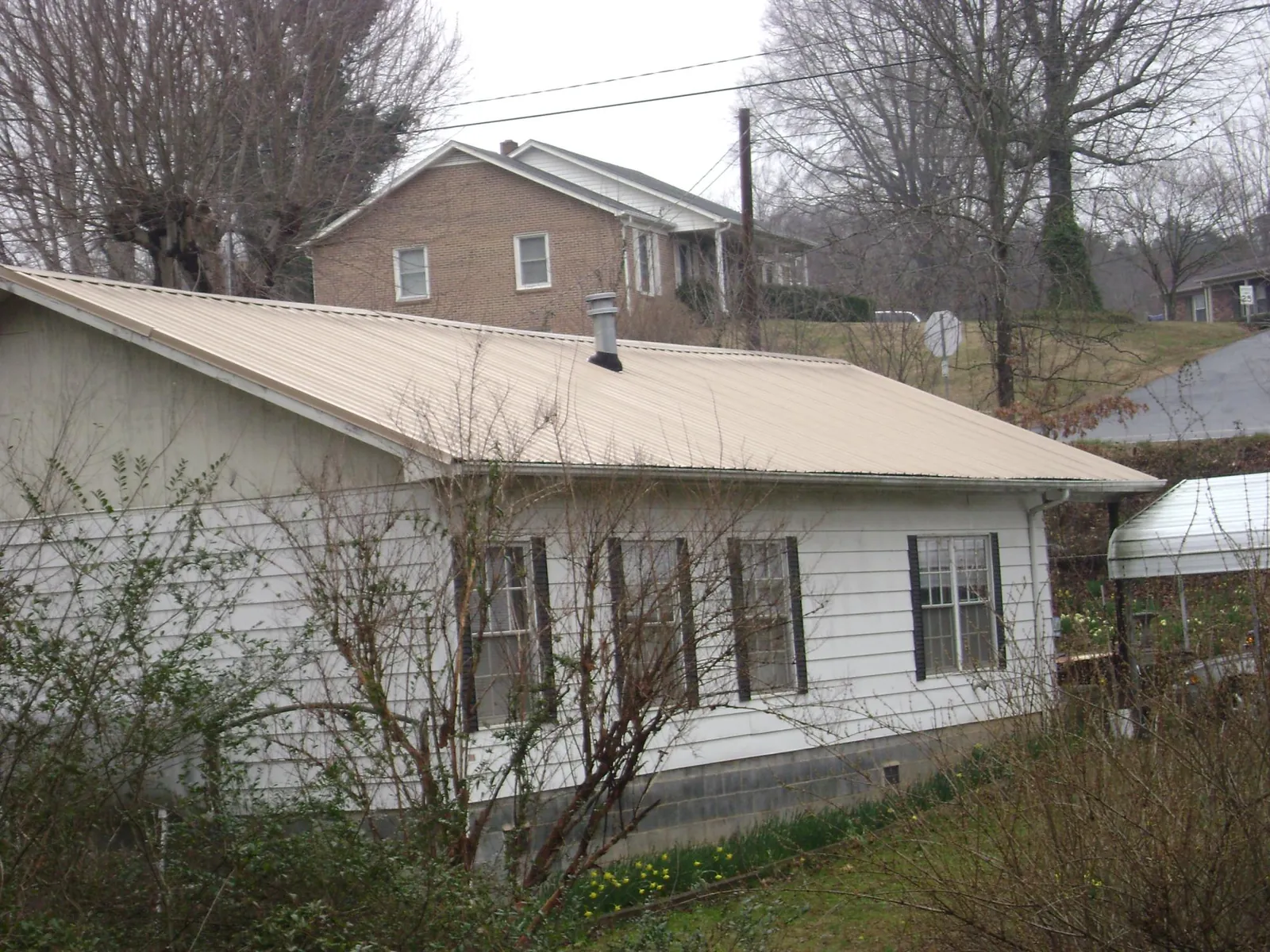 Tan metal roof on a white sided house set into a hillside — Commercial Roofing by Roofing Brothers in Rodessa