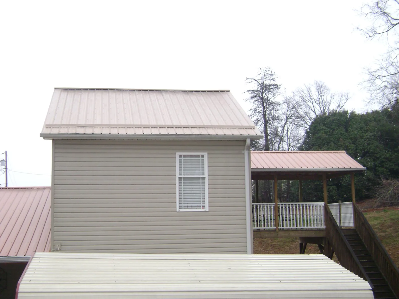 Tan metal roofs on a two story addition and attached porch, from a Roof Replacement job in Rodessa